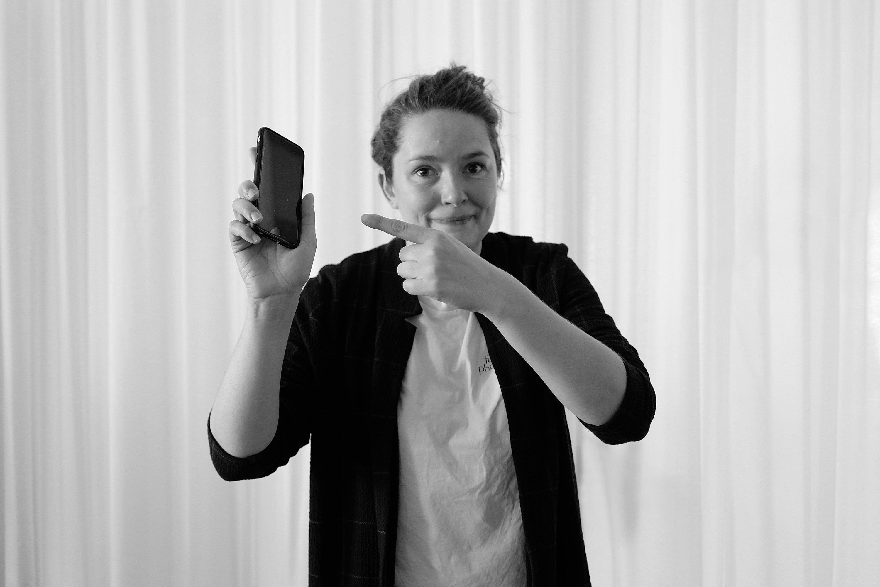 Schwarz-weiß Fotografie von Alex, die mit ihrem Finger auf ihr Handy zeigt