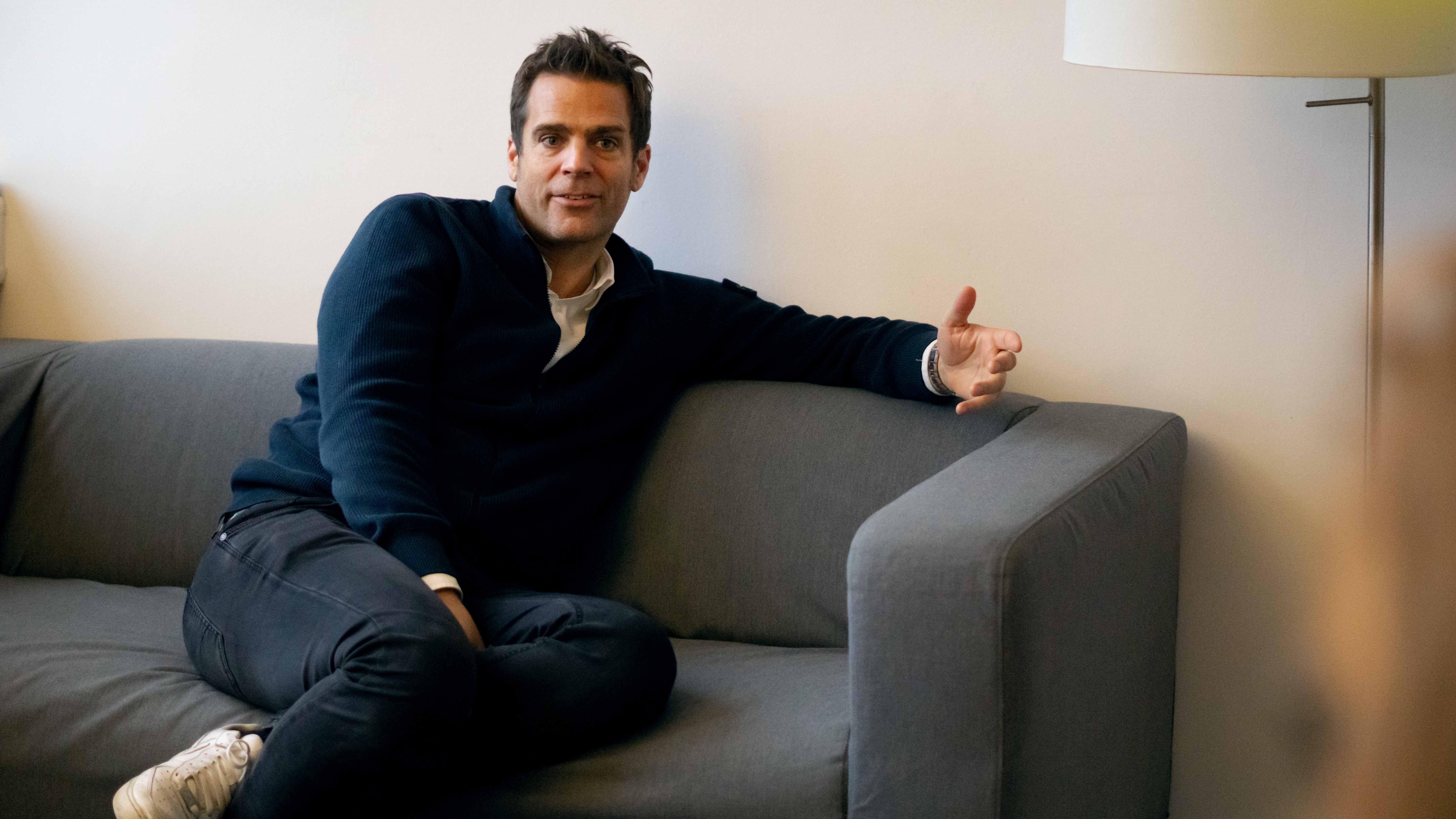 ottomisu CEO Jörn Huber sitzt auf einem grauen Sofa im Büro und führt ein Interview mit Kolleg*innen.