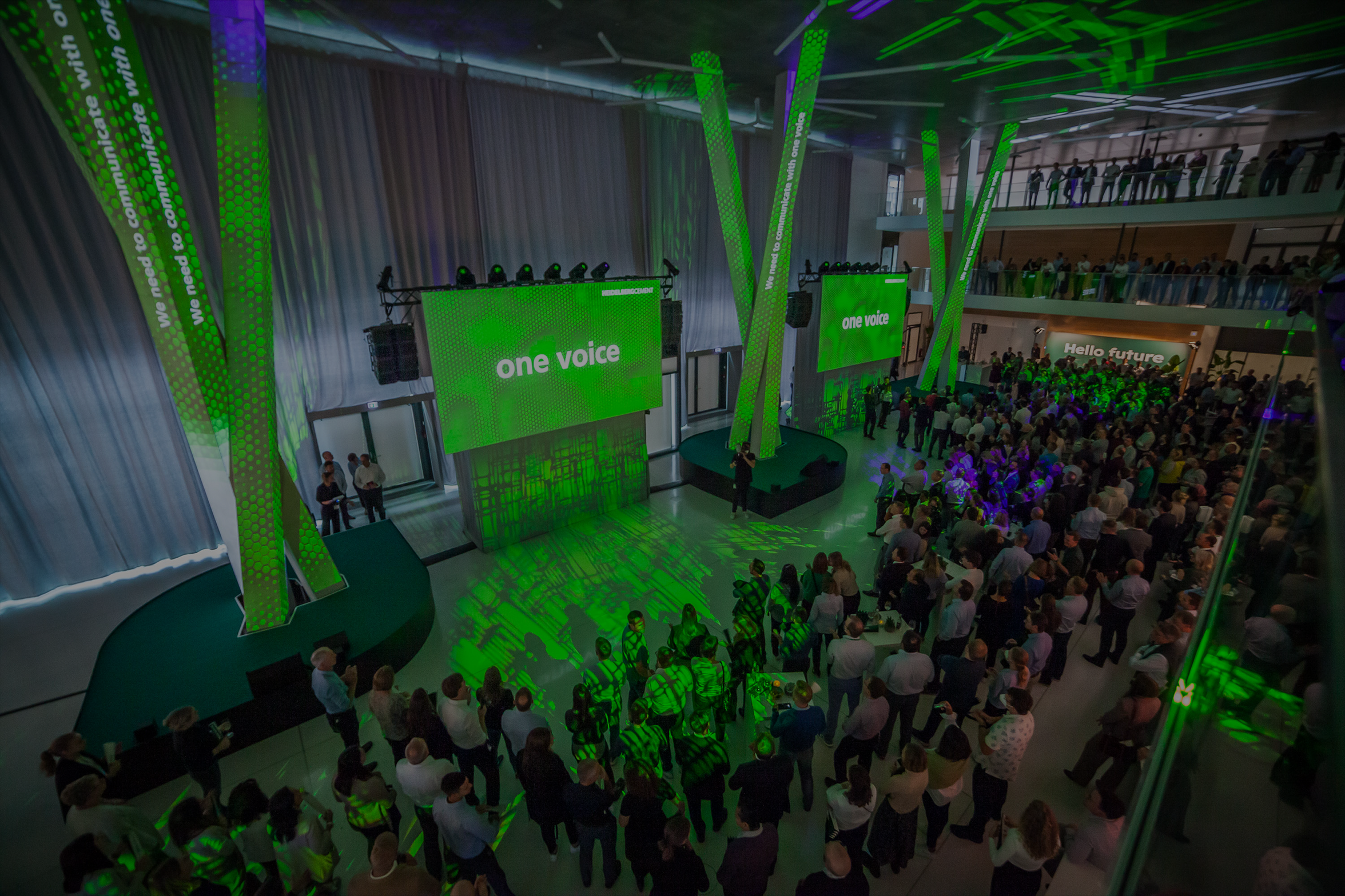 große Veranstaltung in einer modernen Halle mit grüner Beleuchtung, Bühne mit zwei Bildschirmen, auf denen ‚GREEN FUTURE‘ steht, und Publikum.“