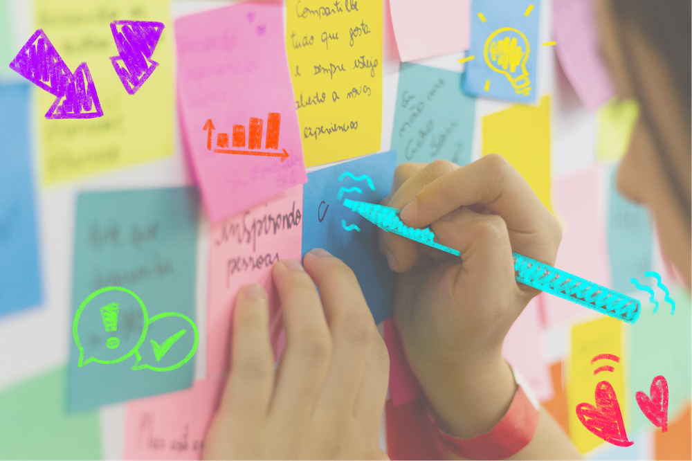 Fotografie von einer Frau, die auf ein Post-It an einer Wand schreibt. Auf das Foto sind bunte Scribbles gezeichnet worden.