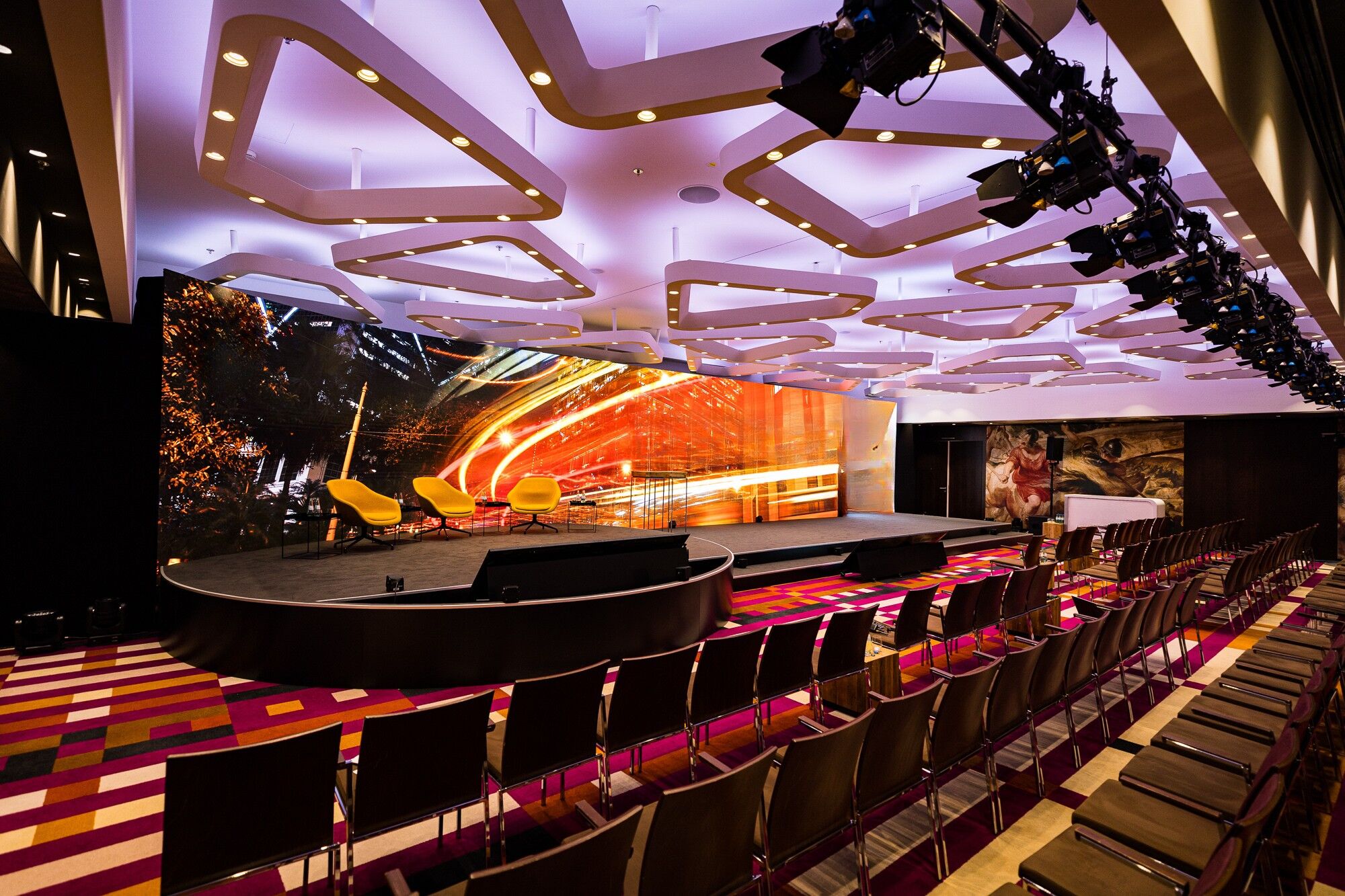 Eventsaal mit LED-Bühne, moderner Lichtdecke und Reihenbestuhlung vor einer großen Multimedia-Leinwand.