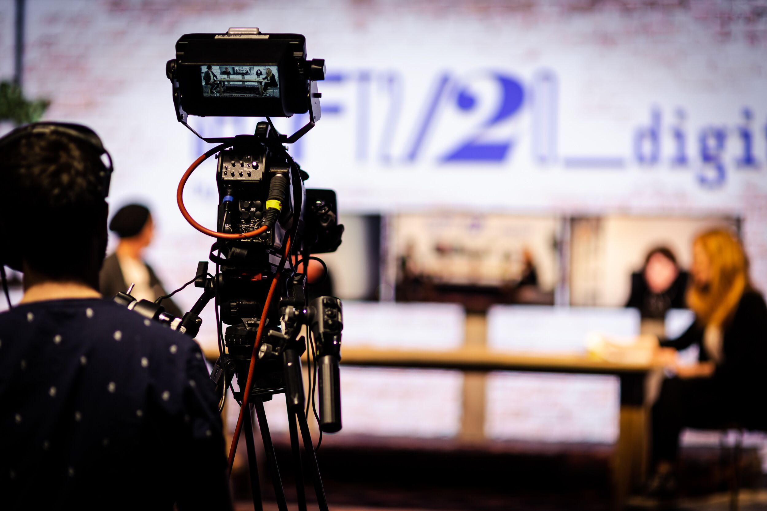 Im Hintergrund ist das Set Up der SHIFT 2020 zu sehen. Im Fokus steht der Kameramann, durch dessen Linse das Set Up betrachtet werden kann.