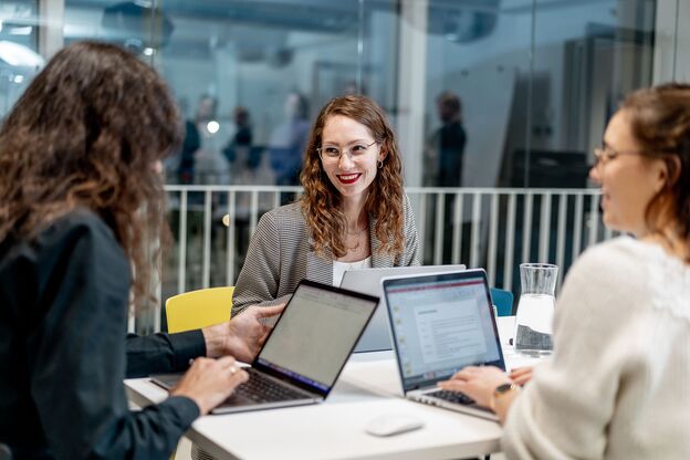 Unser Kollege Sebastian und unsere Kolleginnen Leonie und Elly arbeiten gemeinsam an Laptops in einer offenen Arbeitsumgebung.