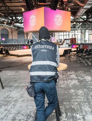 Aufbauarbeiten in einer Industriehalle mit Eventtechnik und Monitoren im Hintergrund.