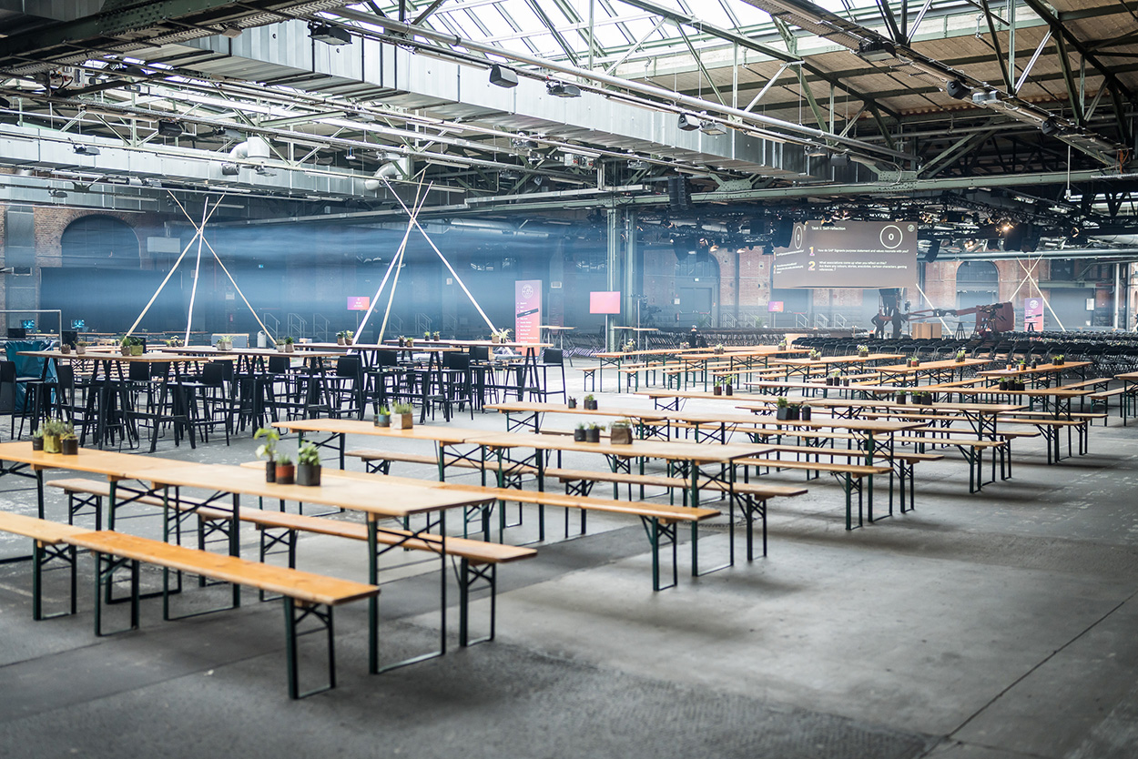 Unser Set-up des Events TO.GATHER SAP Signavio Camp 2023 in der Location Station Berlin. Zu sehen ist eine Halle mit Mischbestuhlung, Tipi-artigen Networking Zonen, Biertischgarnituren und die Bühne.