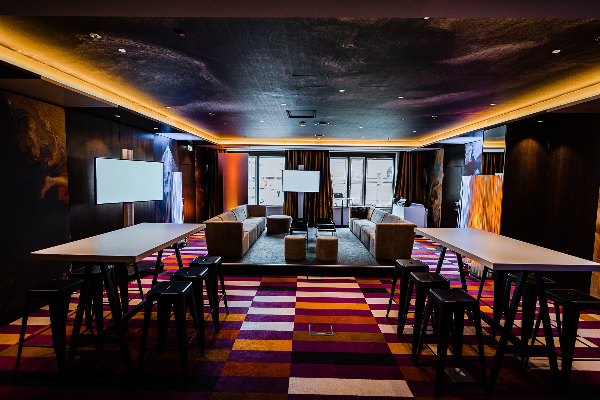 Flexibler Meetingbereich mit Sofas, Stehtischen und Monitoren.