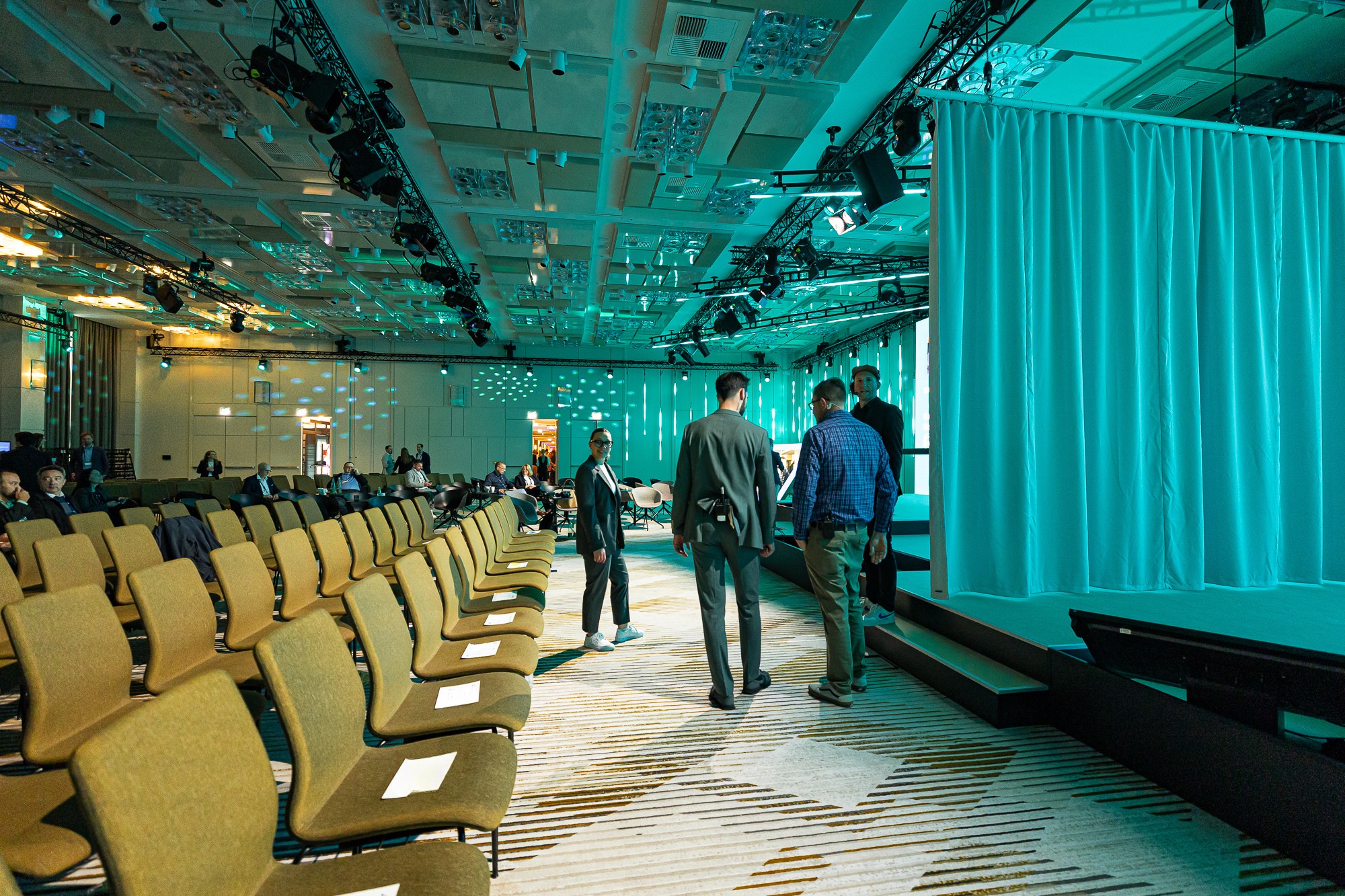 Blick auf Bühne mit großem LED-Screen und moderner Lichtgestaltung, Teilnehmende sitzen in Reihen davor.