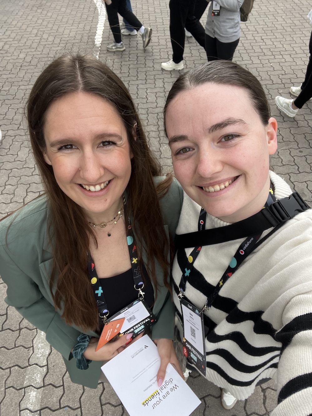 Selfie der zwei OMR-Besucherinnen Sina und Beke an der Garderobe, lachend in die Kamera, mit Festivalbadges um den Hals.