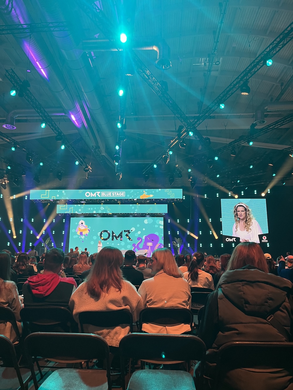 Publikum vor der großen Blue Stage auf der OMR, hellblaues Lichtdesign, Vortrag einer Speakerin auf Bühne und Leinwand.