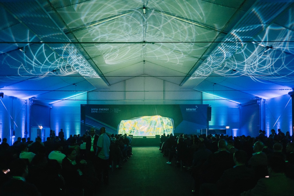 Panoramablick in das Eventzelt während der MWM ENERGY DAYS 2025. Lichtprojektionen an der Decke begleiten die Enthüllung eines Produkts auf der Bühne.
