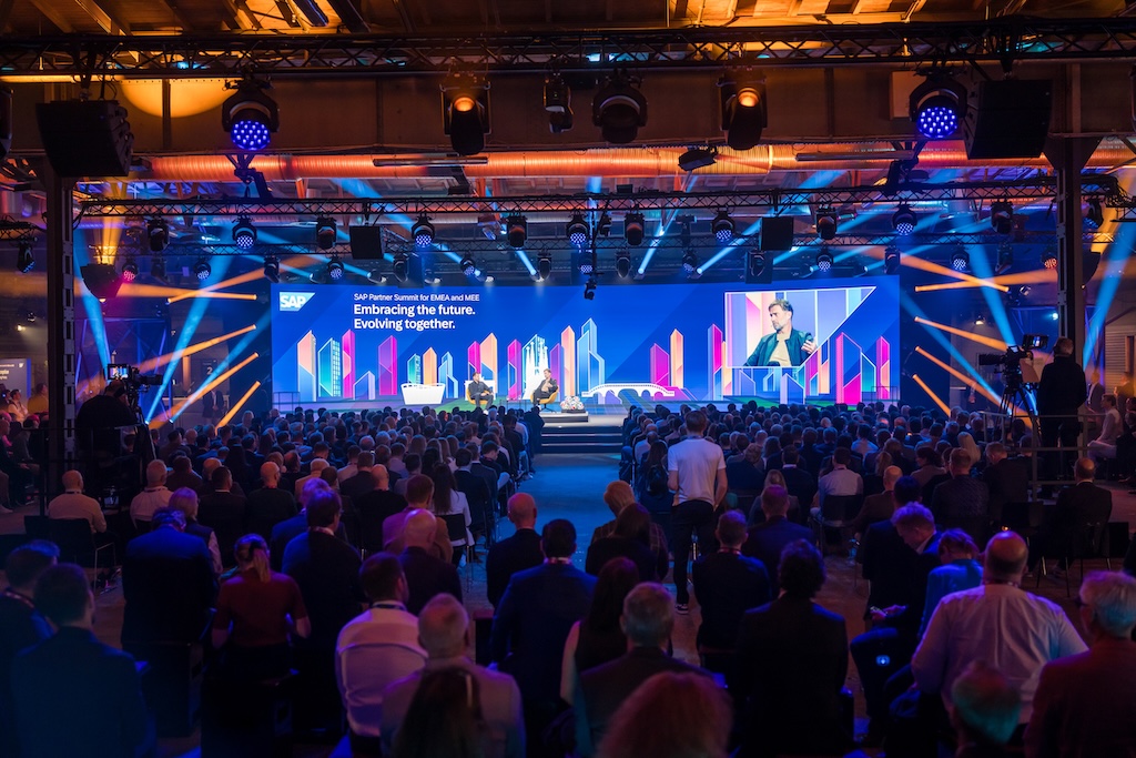 Großaufnahme des Publikums beim Panel-Talk auf der Hauptbühne. Zwei Personen diskutieren, während Visuals mit dem SAP-Motto im Hintergrund leuchten.