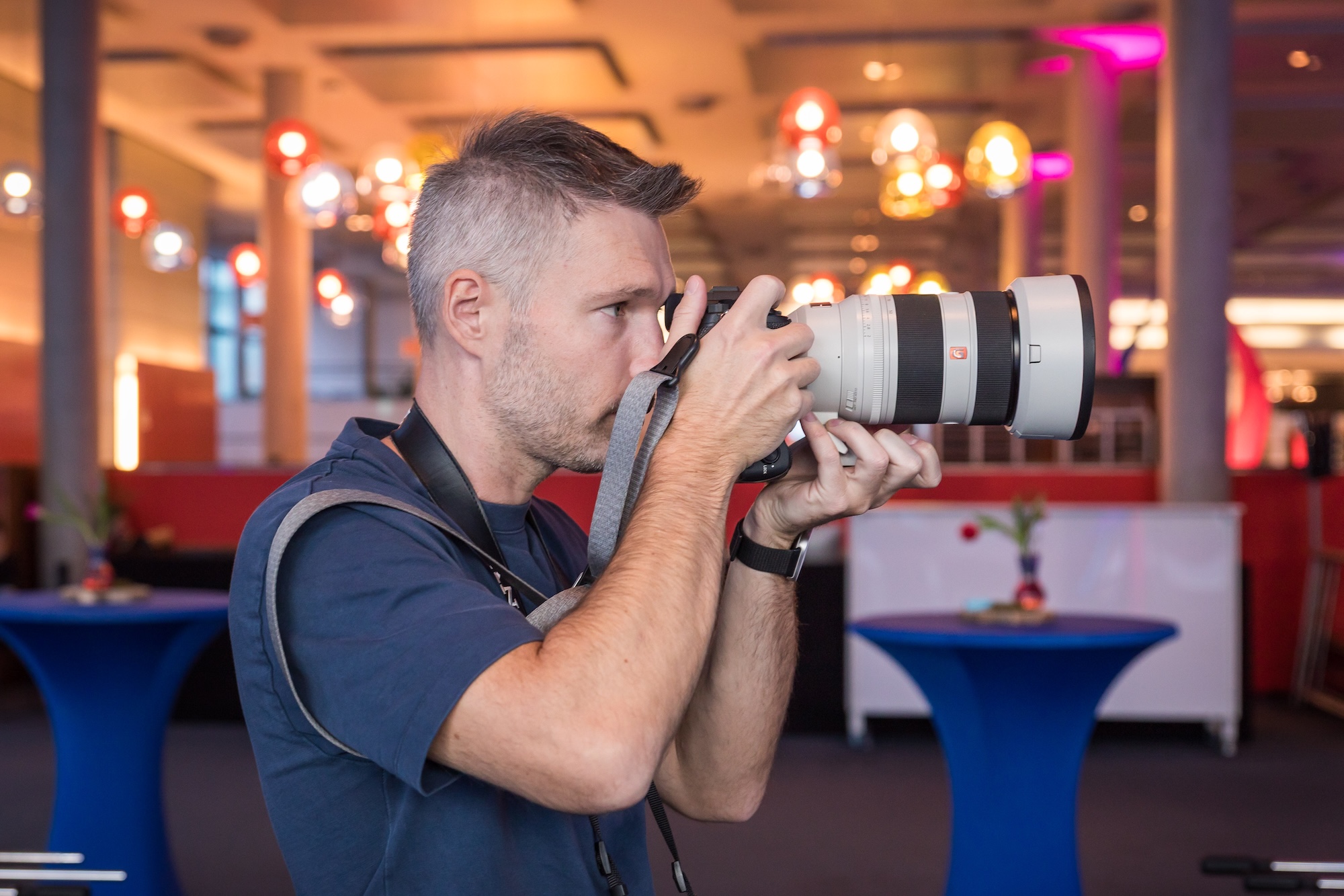Photographer holds a camera to his eye, focusing on a subject in a modern indoor setting.