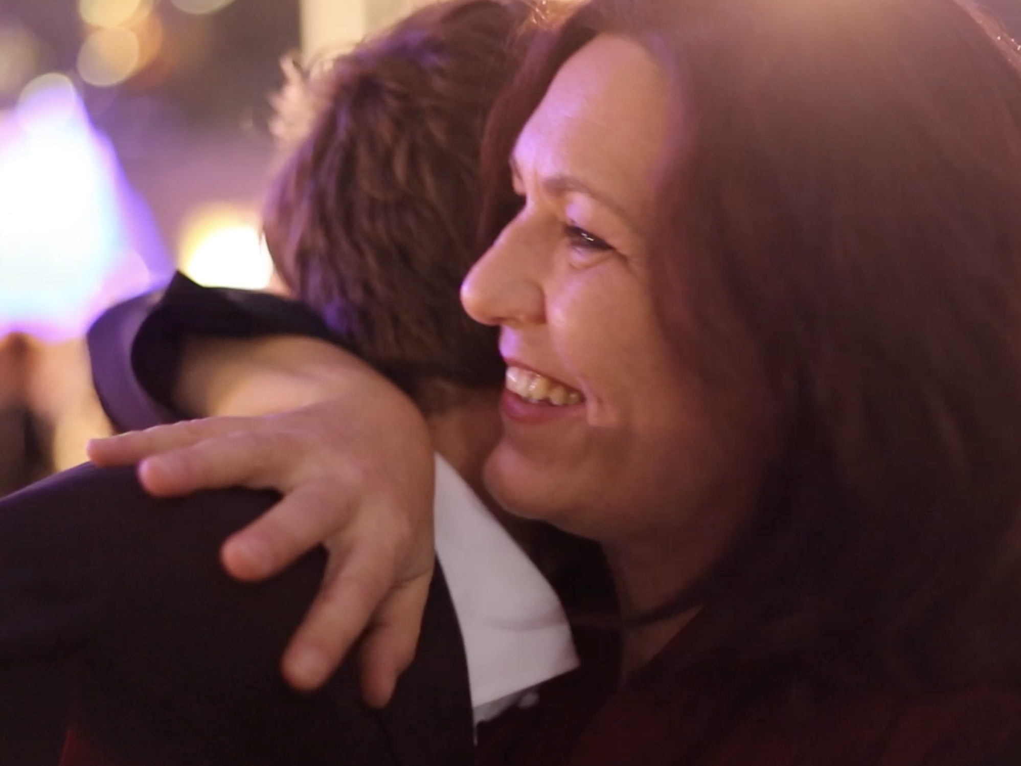 Christine embraces another person at an event, sharing a personal moment of reunion or farewell.