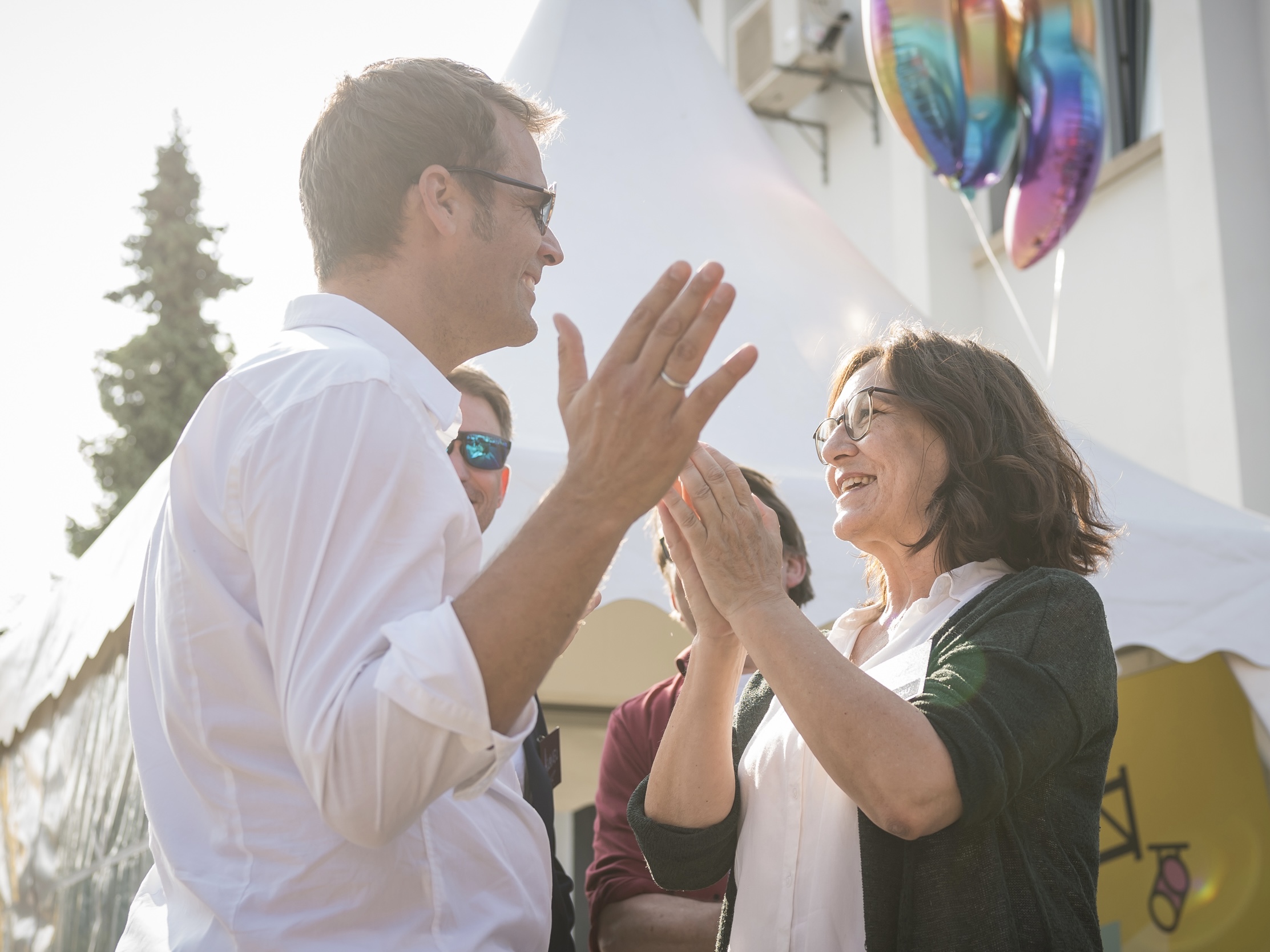 Christine talks with colleagues at an outdoor event in front of event tents and balloons.