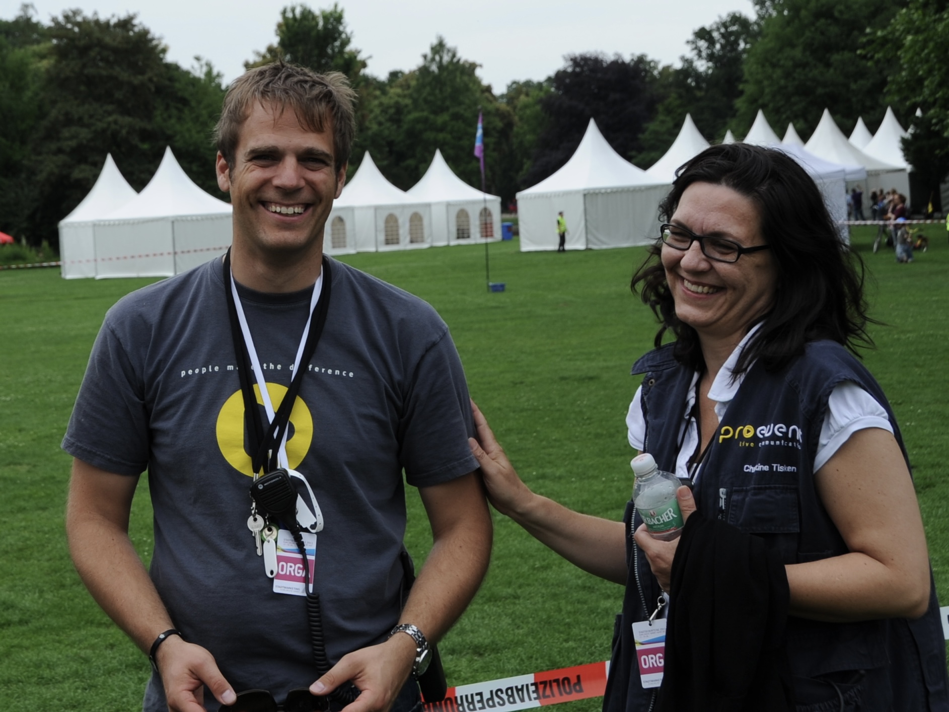 Christine stands with a colleague on an event site in front of event tents, supporting on-site event operations.