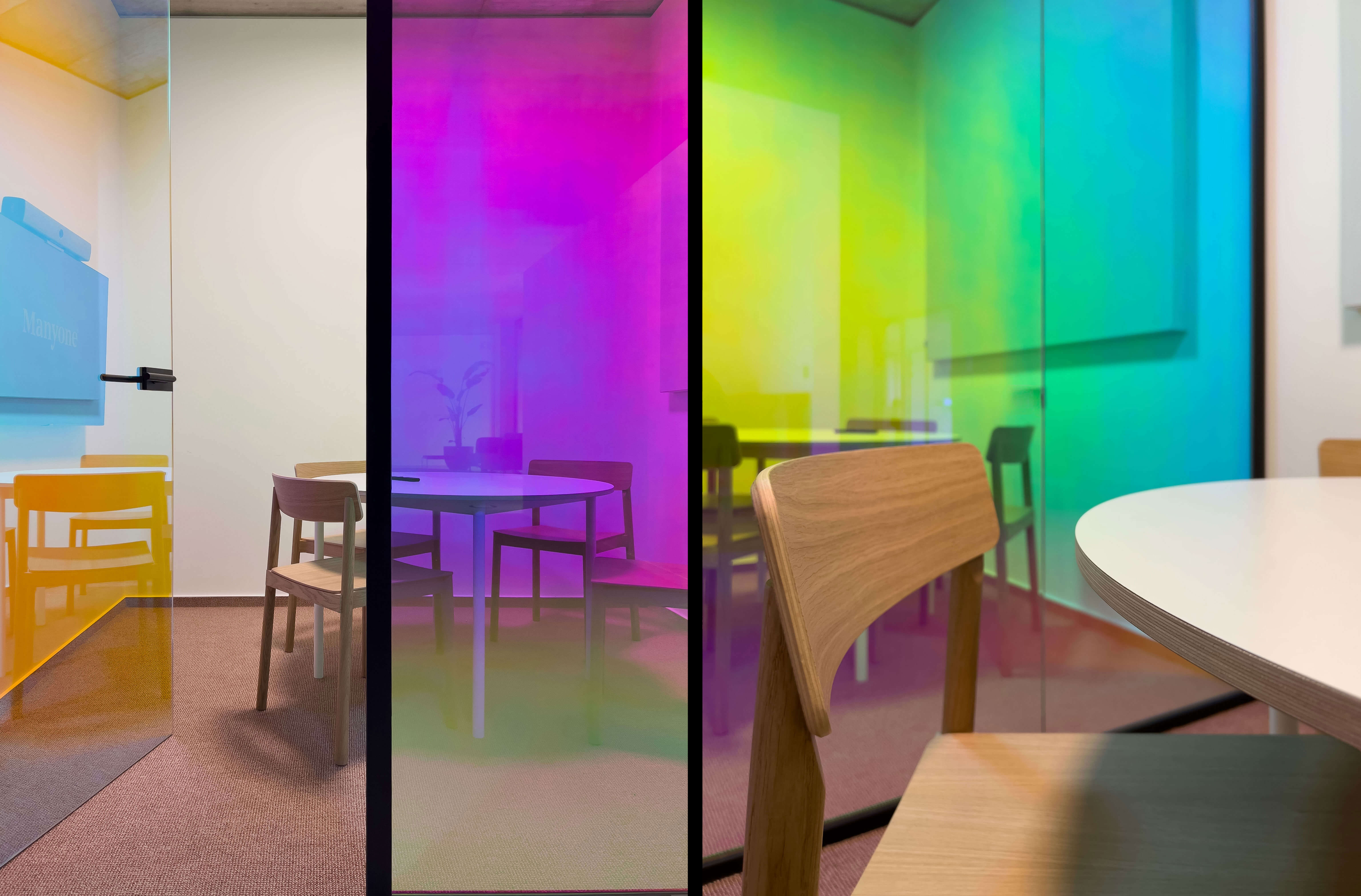 Meeting room with wooden furniture and colored glass walls in shades of yellow, magenta, and green.